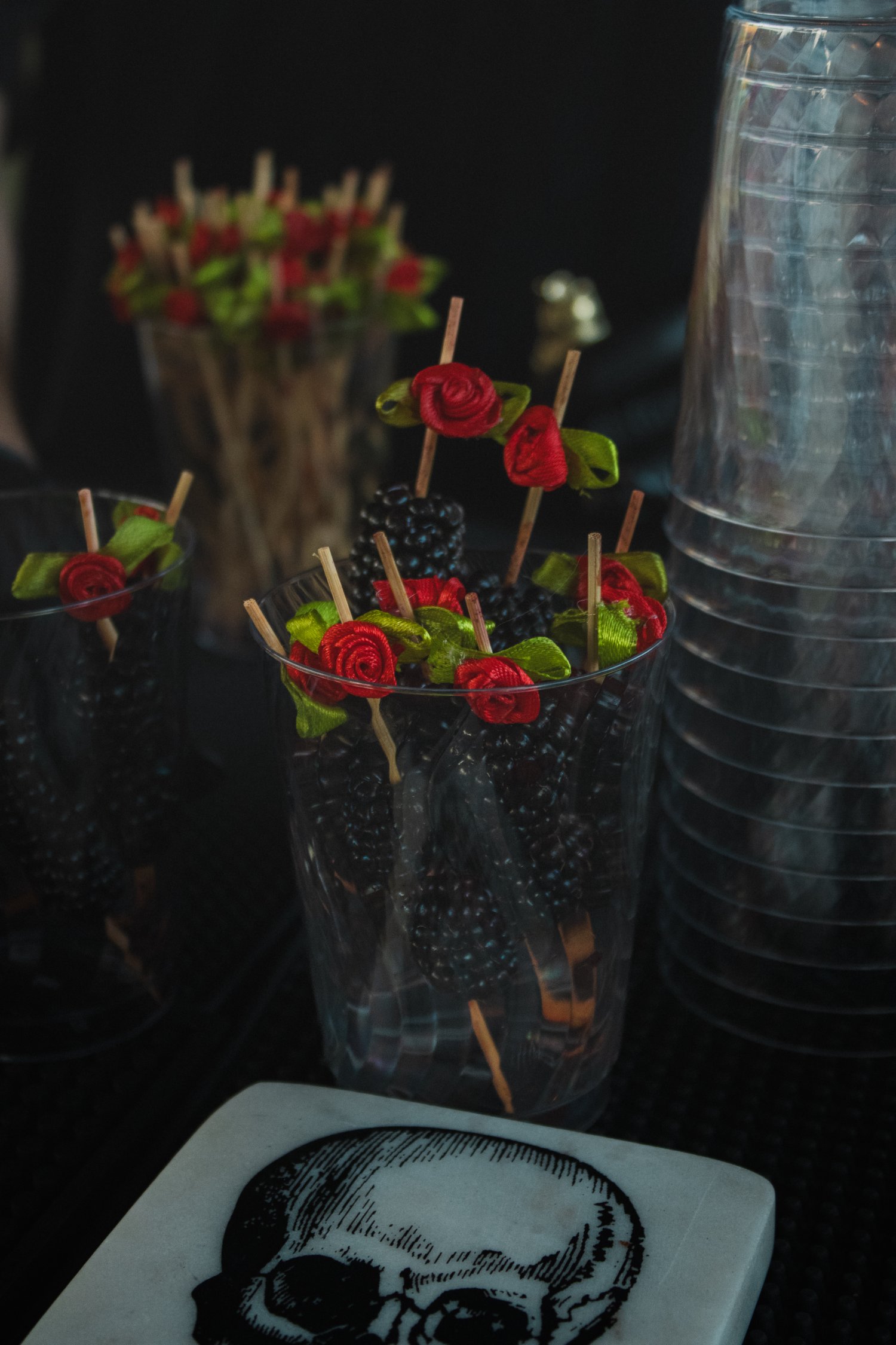 Blackberry garnish picks with red roses beside a skull coaster